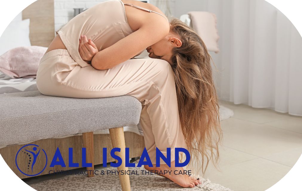 A woman sits on a bench, bent forward with head down and arms around her abdomen, appearing to be in pain—highlighting the need for Back Pain Treatment In Wading River. "ALL ISLAND Chiropractic & Physical Therapy Care" logo is visible.