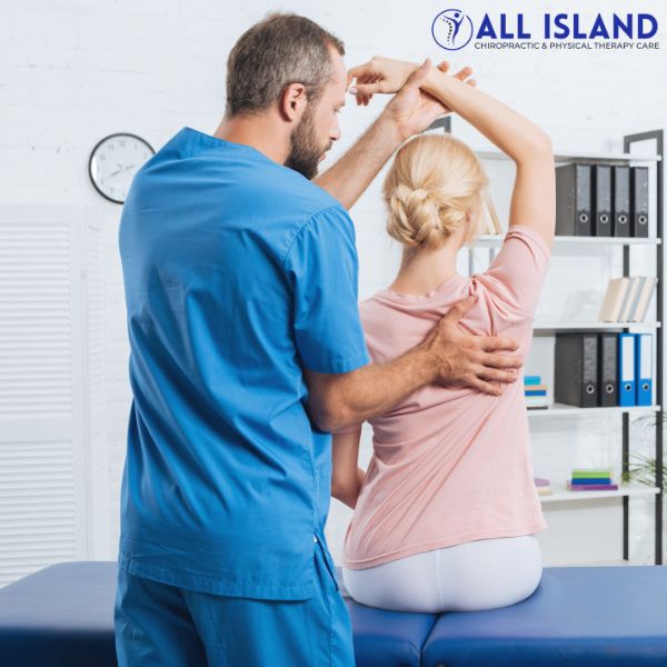 chiropractor brentwood A physical therapist in blue scrubs assists a woman in a pink shirt with a shoulder stretch in a clinic setting, similar to care you’d receive from a chiropractor near Brentwood