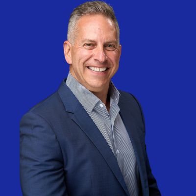 Dr. Craig Selzer Smiling man in a blue suit jacket and striped shirt standing against a solid blue background