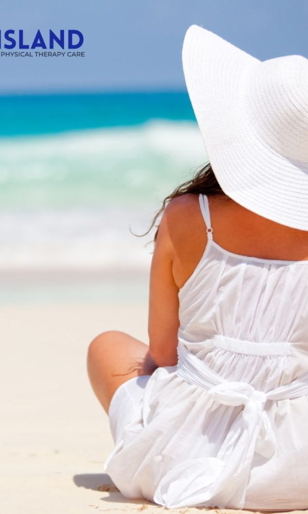 Woman in white dress and sunhat sits on sandy beach facing the ocean; "All Island Chiropractic & Physical Therapy Care" logo in top left corner 