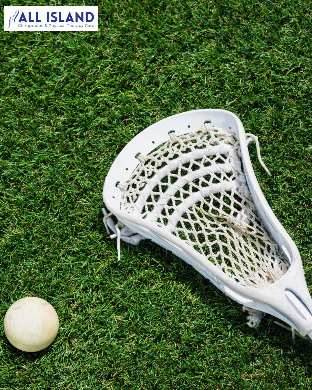 A white lacrosse stick and ball are on green grass. A sign reading “ALL ISLAND Chiropractic & Physical Therapy Care” is in the top left corner.